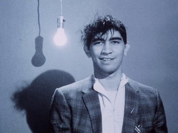 Movie still from “The Decline of Western Civilization” (1981), directed by Penelope Spheeris – A young man in a suit standing in front of a light bulb; Close Up shot, Low angle
