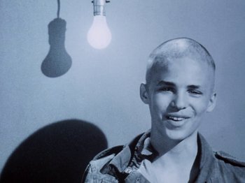 Movie still from “The Decline of Western Civilization” (1981), directed by Penelope Spheeris – A man with a shaved head standing in front of a light bulb; Close Up shot, Low angle