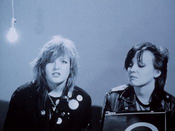 Movie still from “The Decline of Western Civilization” (1981), directed by Penelope Spheeris – A couple of women sitting next to each other on a bench; Close Up shot, Low angle
