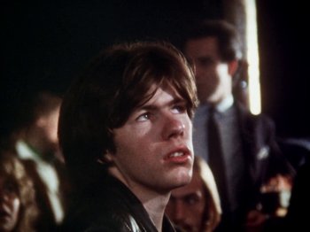Movie still from “The Decline of Western Civilization” (1981), directed by Penelope Spheeris – A young man with long brown hair looking up at the sky; Close Up shot, Over the shoulder angle
