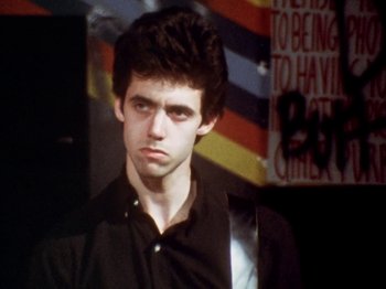 Movie still from “The Decline of Western Civilization” (1981), directed by Penelope Spheeris – A young man in a black dress shirt and black shirt; Close Up shot, Low angle