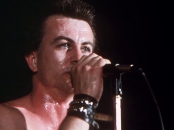 Movie still from “The Decline of Western Civilization” (1981), directed by Penelope Spheeris – A person on a stage with a microphone; Close Up shot, Low angle