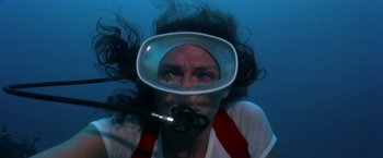 Movie still from “The Deep” (1977), directed by Peter Yates – A woman in a white shirt and a red tie is underwater; Close Up shot, Overhead angle