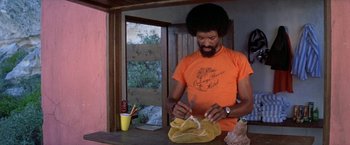 Movie still from “The Deep” (1977), directed by Peter Yates – A man in an orange t - shirt is knitting; Medium shot, Low angle