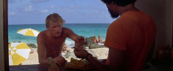 Movie still from “The Deep” (1977), directed by Peter Yates – Two men sitting at a table near the ocean; Medium shot, Low angle