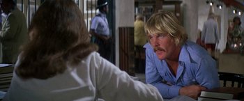 Movie still from “The Deep” (1977), directed by Peter Yates – A man sitting in front of a woman in front of a police officer; Close Up shot, Over the shoulder angle