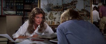 Movie still from “The Deep” (1977), directed by Peter Yates – A woman sitting at a table with papers in front of her; Medium shot, Over the shoulder angle