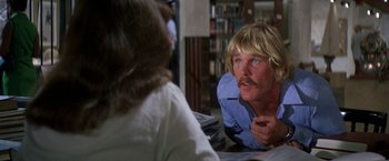 Movie still from “The Deep” (1977), directed by Peter Yates – A man with blonde hair and a mustache talking to a woman in a library; Close Up shot, Over the shoulder angle
