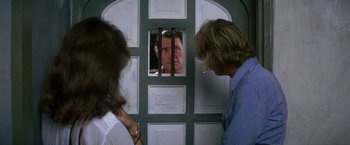Movie still from “The Deep” (1977), directed by Peter Yates – Two people looking at a man through a window; Medium shot, Over the shoulder angle