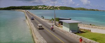 Movie still from “The Deep” (1977), directed by Peter Yates – A man riding a motorcycle down the middle of a road; Extreme Wide shot, High angle