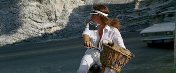 Movie still from “The Deep” (1977), directed by Peter Yates – A woman riding a bicycle down a street; Wide shot, Low angle