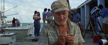 Movie still from “The Deep” (1977), directed by Peter Yates – An older man holding a piece of food in his hands; Medium shot, Over the shoulder angle