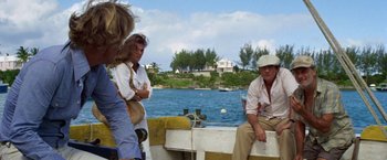 Movie still from “The Deep” (1977), directed by Peter Yates – A group of people sitting on top of a boat in the water; Medium shot, Over the shoulder angle