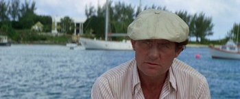 Movie still from “The Deep” (1977), directed by Peter Yates – A person wearing a hat near a body of water; Close Up shot, Low angle