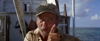 Movie still from “The Deep” (1977), directed by Peter Yates – An old man with a hat and a beard pointing to his ear; Close Up shot, Low angle