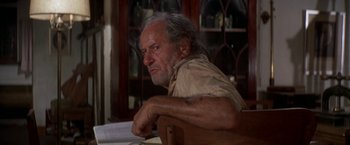 Movie still from “The Deep” (1977), directed by Peter Yates – An older man sitting at a table in front of a window; Close Up shot, Low angle