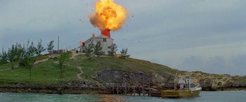 Movie still from “The Deep” (1977), directed by Peter Yates – An explosion erupts from a building on a hill; Extreme Wide shot, Low angle