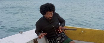 Movie still from “The Deep” (1977), directed by Peter Yates – A man with a beard is sitting in a boat; Medium shot, Low angle