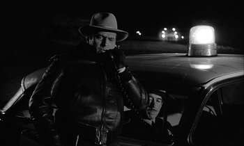 Movie still from “The Defiant Ones” (1958), directed by Stanley Kramer – A man talking on a phone next to another man in a car at night; Medium shot, Low angle