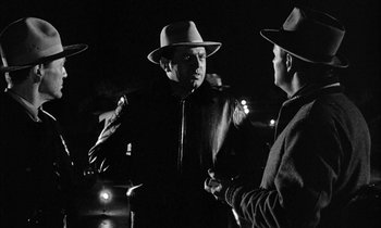 Movie still from “The Defiant Ones” (1958), directed by Stanley Kramer – A man in a hat talking to another man in a hat; Medium shot, Over the shoulder angle