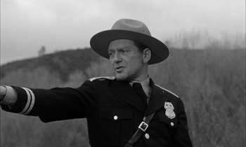 Movie still from “The Defiant Ones” (1958), directed by Stanley Kramer – A man in a police officer's uniform pointing to the sky; Medium shot, Low angle