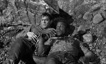 Movie still from “The Defiant Ones” (1958), directed by Stanley Kramer – Two men are laying on the ground in a cave; Medium shot, High angle
