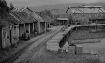 Movie still from “The Defiant Ones” (1958), directed by Stanley Kramer – An old photo of some buildings and a dock; Extreme Wide shot, High angle