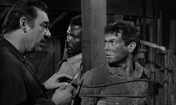 Movie still from “The Defiant Ones” (1958), directed by Stanley Kramer – A man is holding a pair of scissors in his hand; Medium shot, Over the shoulder angle