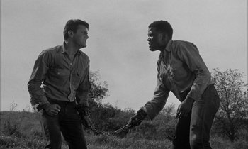 Movie still from “The Defiant Ones” (1958), directed by Stanley Kramer – Two men in a field one of them is holding a chain; Medium shot, Low angle