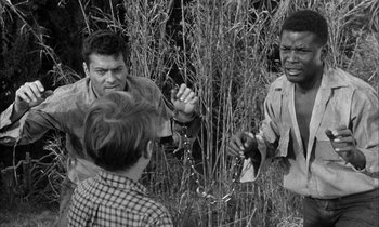Movie still from “The Defiant Ones” (1958), directed by Stanley Kramer – A group of people standing in tall grass; Medium shot, Over the shoulder angle
