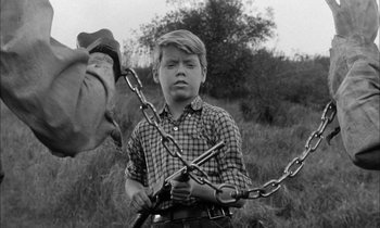 Movie still from “The Defiant Ones” (1958), directed by Stanley Kramer – A young boy holding a chain in his hands; Medium shot, Over the shoulder angle