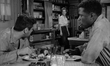 Movie still from “The Defiant Ones” (1958), directed by Stanley Kramer – A woman standing in front of two men at a table; Medium shot, Over the shoulder angle