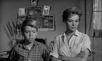 Movie still from “The Defiant Ones” (1958), directed by Stanley Kramer – A woman and a young boy are standing next to each other in a living room; Medium shot, Over the shoulder angle