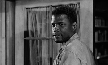 Movie still from “The Defiant Ones” (1958), directed by Stanley Kramer – A black and white photo of a man standing in front of a window; Close Up shot, Low angle
