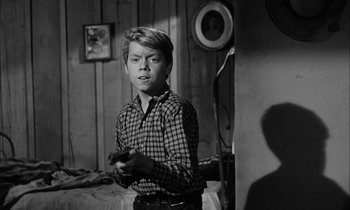 Movie still from “The Defiant Ones” (1958), directed by Stanley Kramer – A young man holding a wii controller in a room; Medium shot, Over the shoulder angle