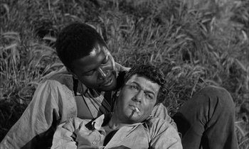 Movie still from “The Defiant Ones” (1958), directed by Stanley Kramer – Two men sitting on the ground one is smoking a cigarette and the other is leaning on the shoulder of another man; Close Up shot, Over the shoulder angle