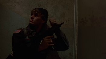 Movie still from “The Delta Force” (1986), directed by Menahem Golan – A man holding a gun in a room; Medium shot, Low angle