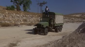 Movie still from “The Delta Force” (1986), directed by Menahem Golan – A man sitting on top of the back of an army truck; Wide shot, High angle