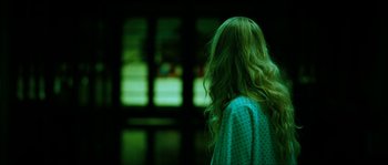 Movie still from “The Descent” (2005), directed by Neil Marshall – A woman with long green hair standing in front of a window; Medium shot, Over the shoulder angle