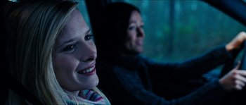 Movie still from “The Descent” (2005), directed by Neil Marshall – Two people sitting in a car smiling for the camera; Close Up shot, Over the shoulder angle