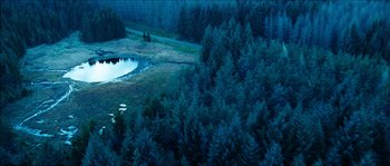Movie still from “The Descent” (2005), directed by Neil Marshall – A view from above of a pond in a wooded area at night; Extreme Wide shot, High angle