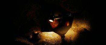 Movie still from “The Descent” (2005), directed by Neil Marshall – A woman with a headlamp looking down at the ground; Close Up shot, High angle