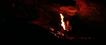 Movie still from “The Descent” (2005), directed by Neil Marshall – A man sitting in front of a fire in a cave; Wide shot, High angle
