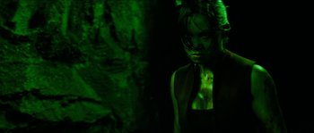 Movie still from “The Descent” (2005), directed by Neil Marshall – A woman in a black top is standing in front of a rock wall; Medium shot, Over the shoulder angle