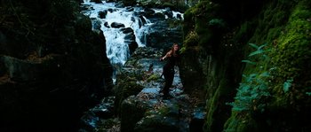 Movie still from “The Descent” (2005), directed by Neil Marshall – A woman standing on a rock near a waterfall; Wide shot, High angle