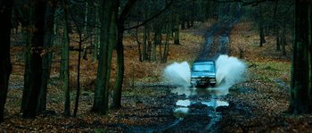 Movie still from “The Descent” (2005), directed by Neil Marshall – A car driving through a puddle on a muddy road; Extreme Wide shot, High angle