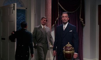 Movie still from “The Devil Rides Out” (1968), directed by Terence Fisher – A man in a suit and tie standing next to another man in a suit and tie; Medium shot, Low angle