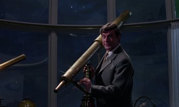 Movie still from “The Devil Rides Out” (1968), directed by Terence Fisher – A man in a suit and tie holding a telescope; Medium shot, Low angle