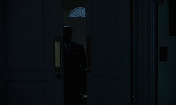 Movie still from “The Devil Rides Out” (1968), directed by Terence Fisher – A man in a suit standing in front of an open door at night; Wide shot, Over the shoulder angle