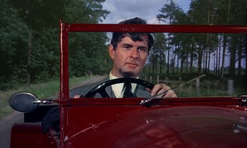 Movie still from “The Devil Rides Out” (1968), directed by Terence Fisher – A man driving a red car in a forest; Close Up shot, Over the shoulder angle